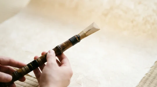 Traditional hichiriki double-reed bamboo flute held by hands with natural reed visible against minimalist background