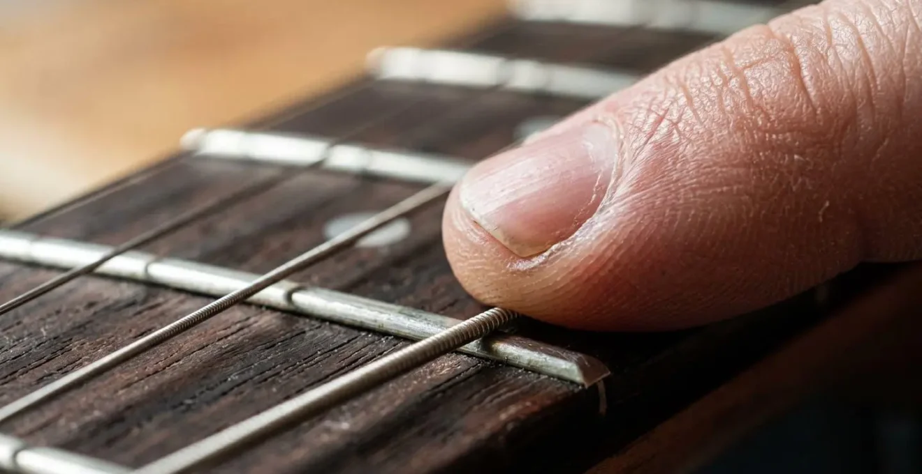Macro photograph of a guitar fretboard showing the tension of a finger pressing a string, with very shallow depth of field