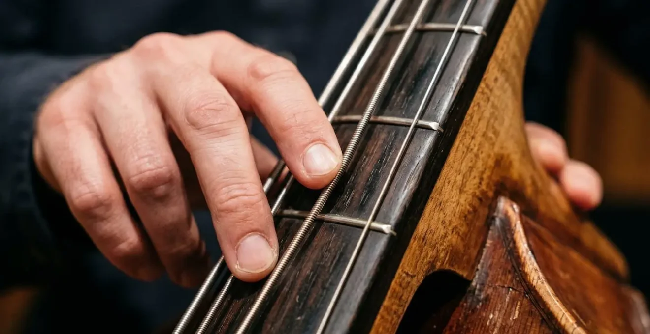 Extreme close-up of a double bass player's fingers on strings with shallow depth of field, capturing the tactile texture of strings and wood grain in warm studio lighting