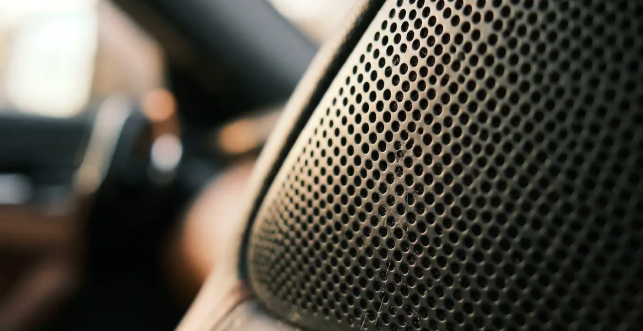 Macro view of car dashboard speaker grille with shallow depth of field emphasizing acoustic texture