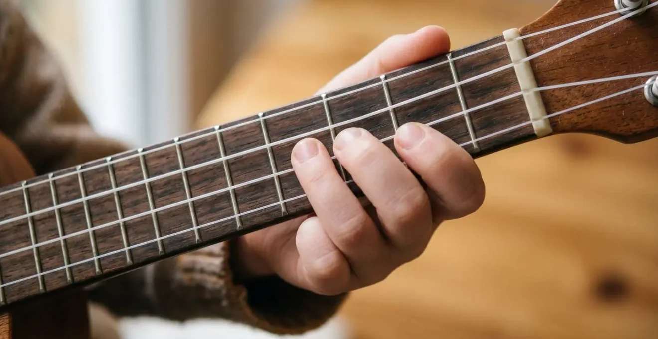 Close-up of child's small hands positioned on ukulele fretboard showing comfortable finger placement