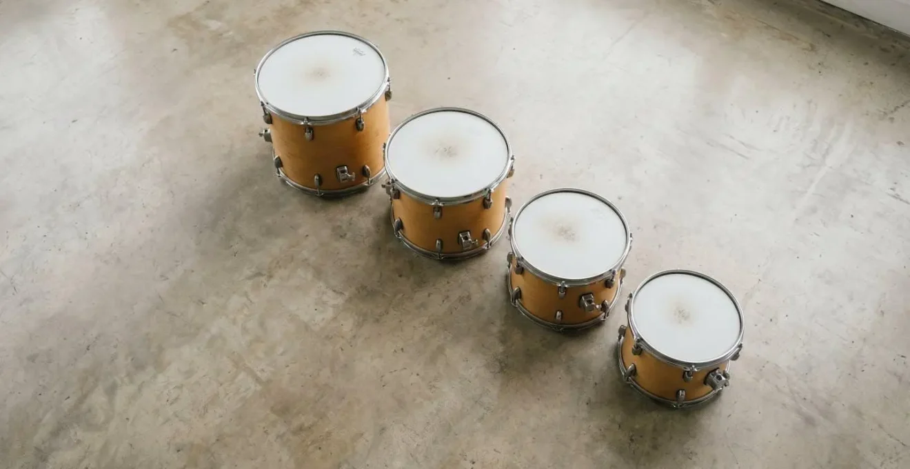 Overhead wide shot of tuned tom drums arranged in descending musical intervals with minimal staging and natural ambient light