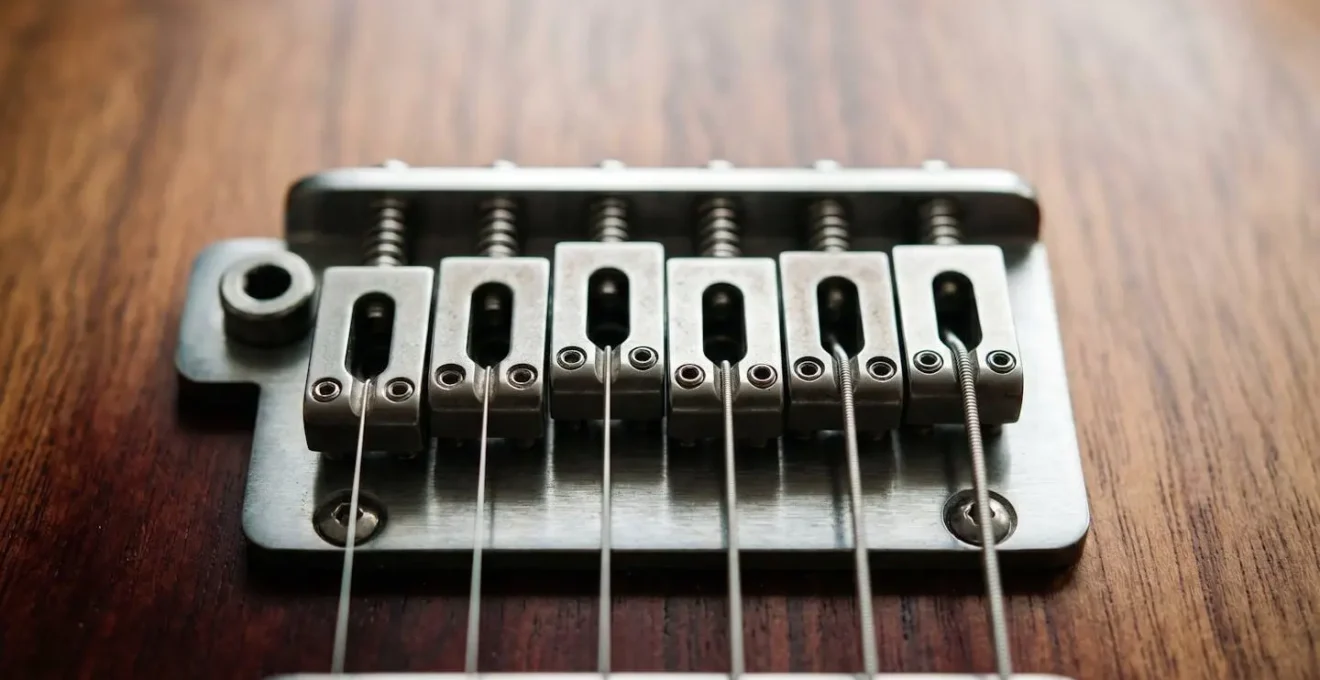Close-up photograph of an electric guitar bridge showing individual saddle adjustments with precision hardware details
