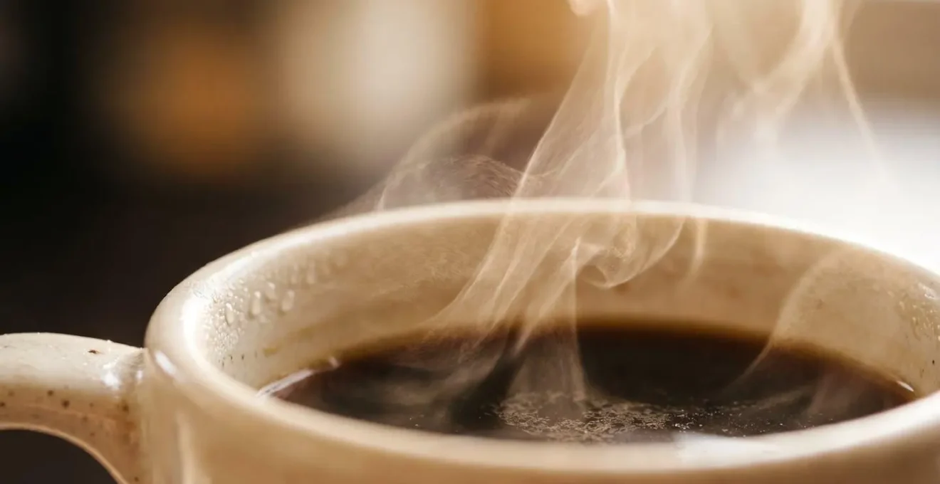 Extreme close-up macro shot of steam rising from dark coffee surface with condensation droplets on ceramic rim