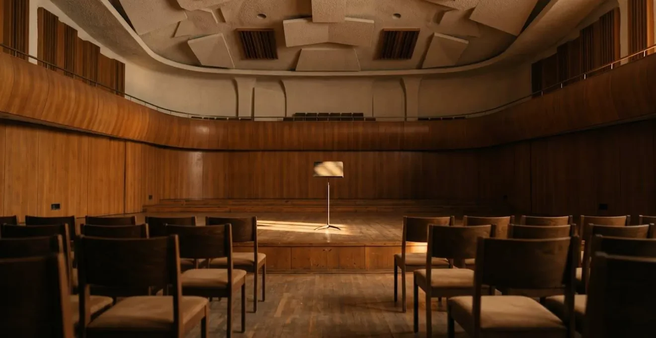 Wide environmental shot of empty concert hall with single music stand in warm afternoon light